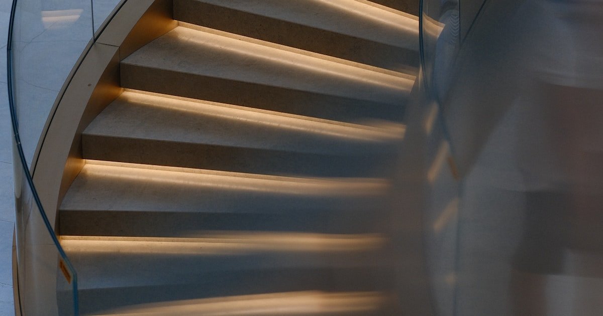 Spiral staircase with glass railing and warm lighting